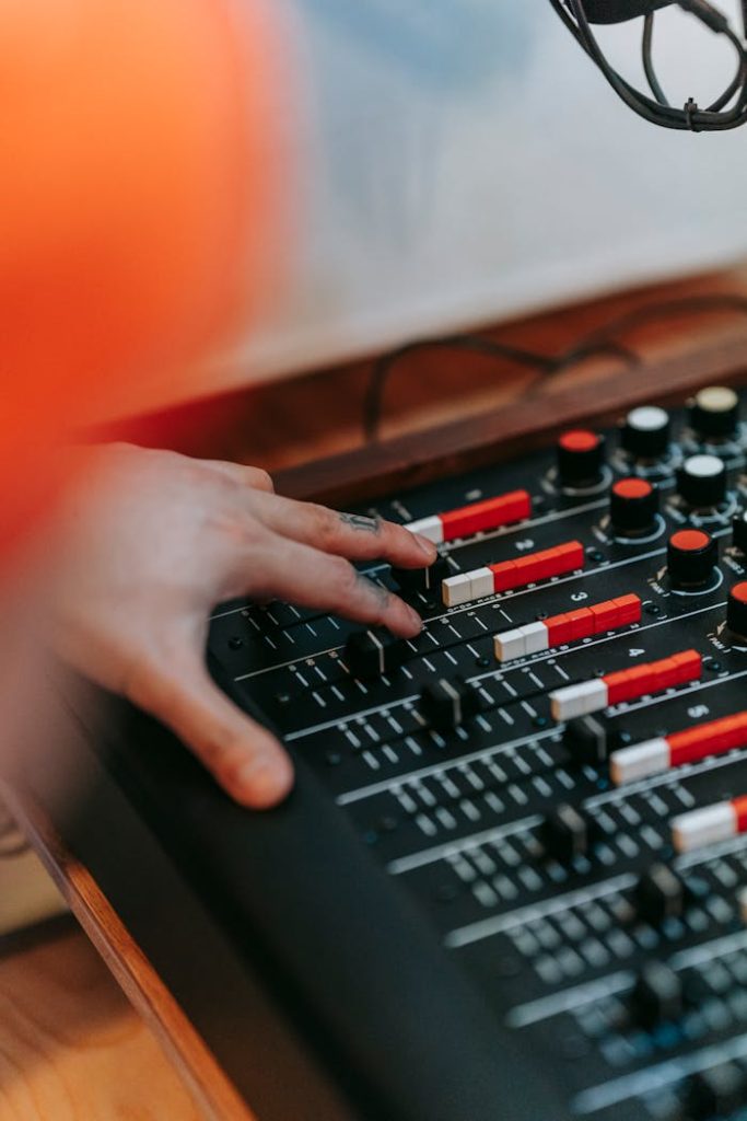 A person adjusts knobs and sliders on a professional audio mixer in a recording studio setting.